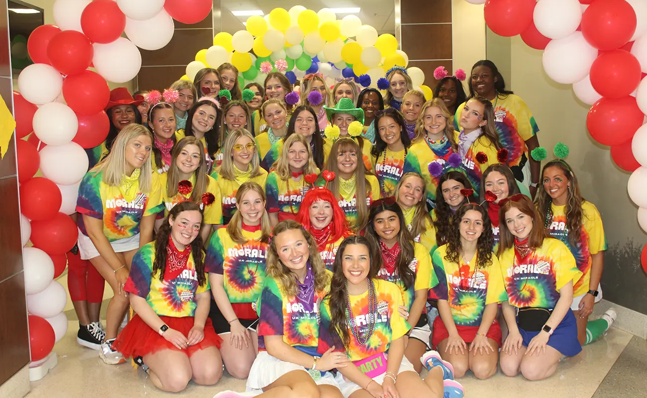 Students under balloon arch wearing UA Miracle Morale tie-dyed t-shirts